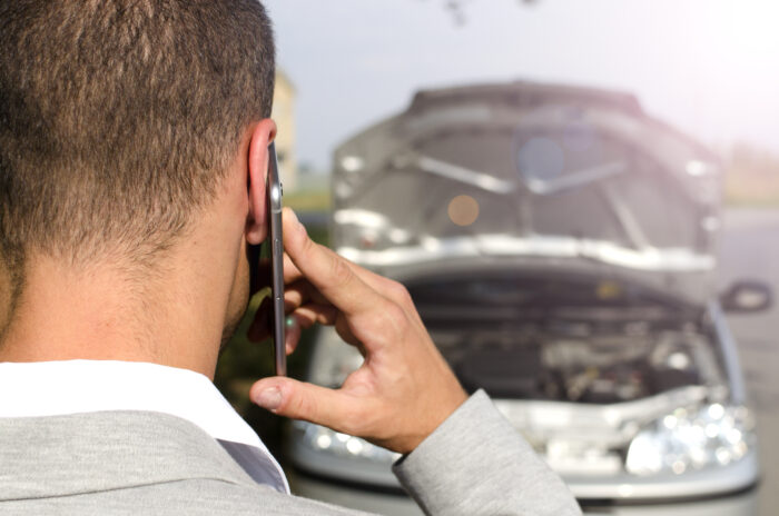 man standing by broken vehicle calling tow service