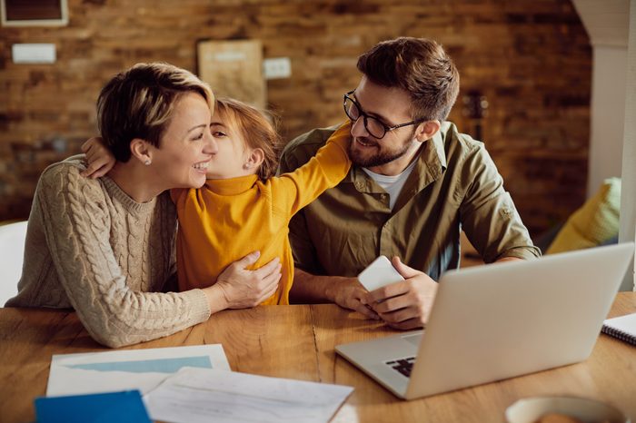 happy daughter embracing kissing her working parents home