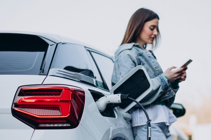 Auto elettriche a noleggio a lungo termine: convengono? woman charging her electric car with charging pistol